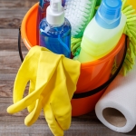 Plastic bucket with cleaning supplies on wood background