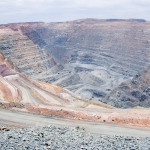 Big mine pit with little dump trucks and reddish soil