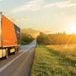 Truck driving on the asphalt road in rural landscape at the golden sunset