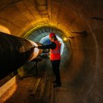 Tunnel worker examines pipeline in underground tunnel