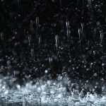 Heavy rain falling down on ground against dark background