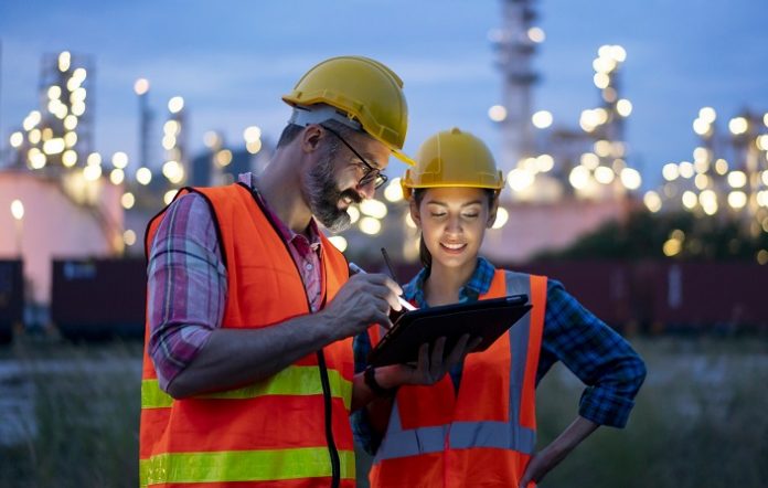 Engineer using tablet near oil refinery at night.