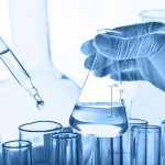 Flask in scientist hand with lab glassware background