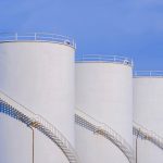 Three white storage fuel tanks in petroleum industry area agains