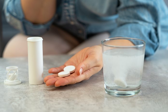Womens hands with pills and water glass with effervescent tablet. Soluble drug