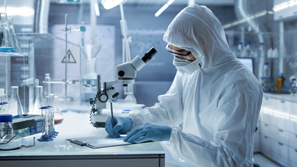 In a Secure High Level Laboratory Scientists in a Coverall Conducting a Research. Chemist Adjusts Samples in a Petri Dish with Pincers.